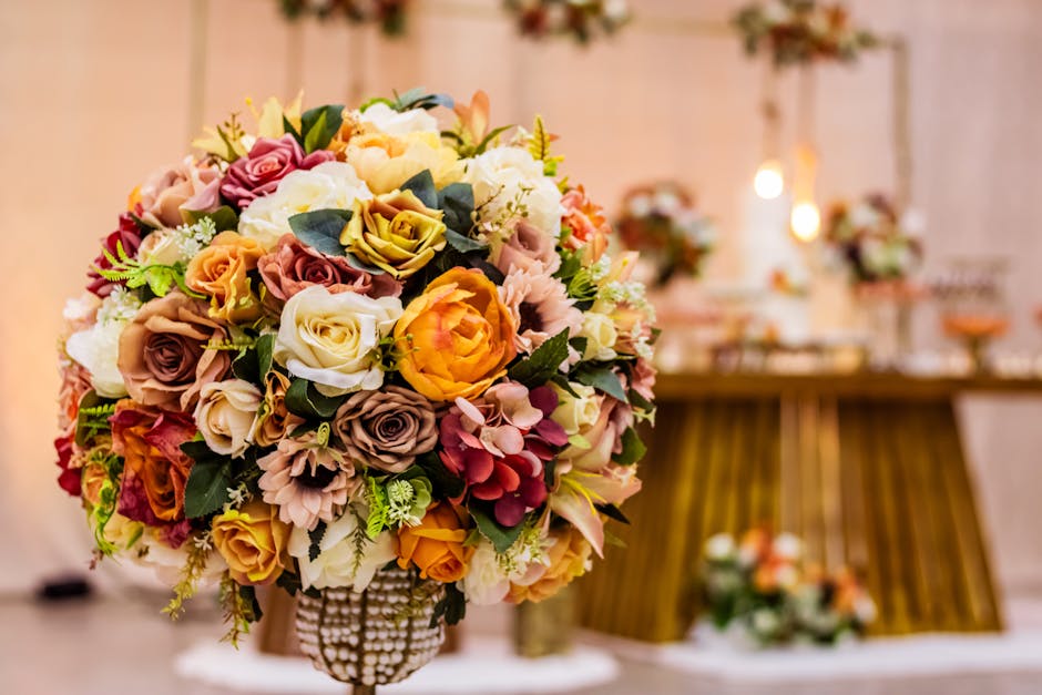 A large, round floral bouquet featuring a mix of fresh roses, peonies, and hydrangeas in shades of pink, peach, cream, and lavender, accented with green foliage. The bouquet is arranged in a decorativ